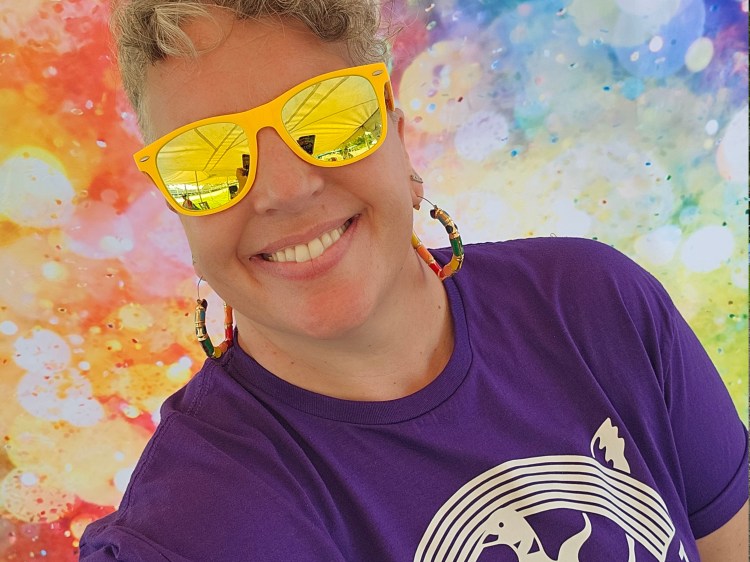 Smiling femme in yellow sunglasses in front of rainbow spatter